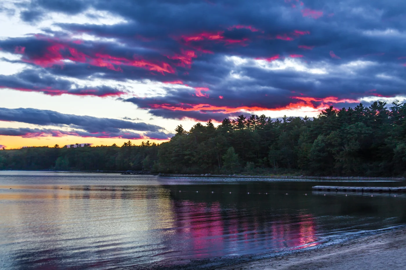 Sunset over Sebago Lake in Maine, with pine-covered shoreline and reflections on the water